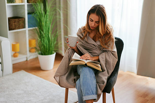 istock Young woman reading a book and drinking tea at home 2232970562