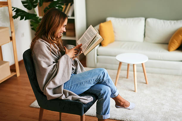 istock Smiling woman relaxing at home reading a book and drinking tea 2232970663