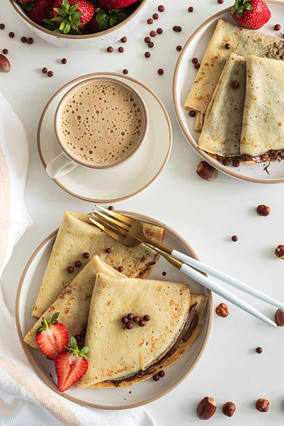istock Crepes with chocolate hazelnut spread, strawberries and hazelnuts on a white wooden table. Top view 2232976636