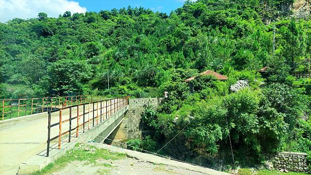 istock Bridge with rusty guardrail in lush green forested hills under clear sky 2232980498
