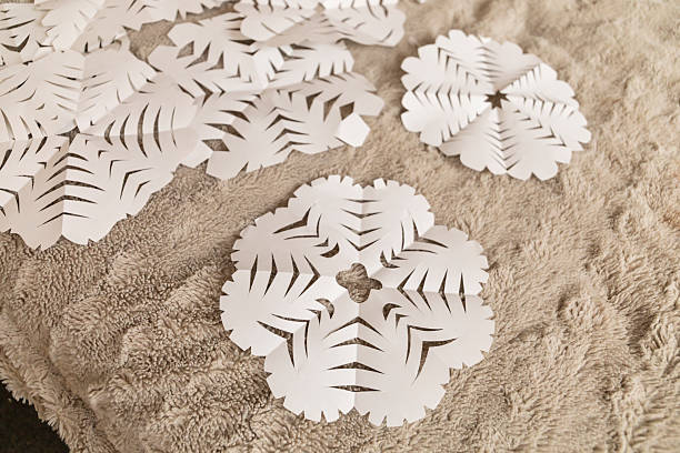 istock Delicate paper snowflakes are arranged on a soft, textured surface, showcasing detailed cut patterns in a creative winter crafting activity. The cozy environment enhances the crafting mood 2232982663