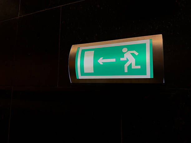 istock Illuminated green emergency exit sign on dark wall with arrow pointing left 2232982727
