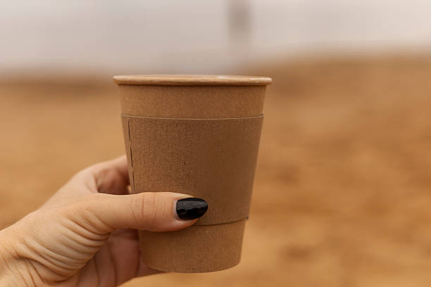istock A person with painted nails enjoys a warm beverage from a disposable cup, surrounded by earthy tones of a sandy environment under soft natural light 2232984068