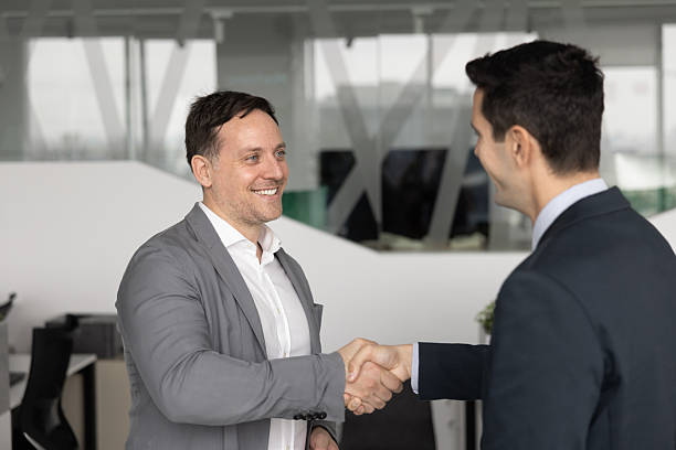 istock Two smiling businessmen standing in office, shaking hands 2232984601