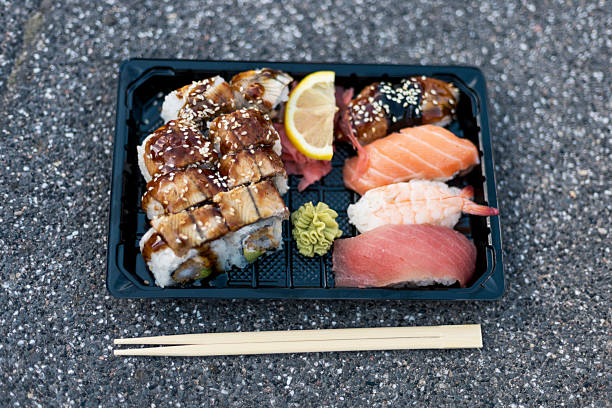 A beautifully arranged platter of sushi includes eel, salmon, and tuna pieces along with fresh ginger, wasabi, and a lemon slice, set on a textured surface
