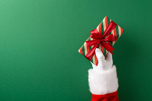 istock A Santa's hand in a festive red suit holding a neatly wrapped gift with a bow 2232991904