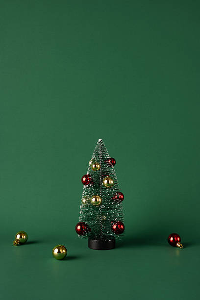 istock Small vertical decorative Christmas tree adorned with red and gold ornaments, set on a green background. Perfect for holiday greeting cards, festive decorations, or Merry Christmas themed purposes 2232991953