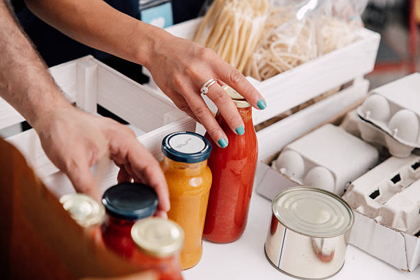 Close-up of volunteers’ hands as they organize jars of sauces, canned goods, pasta, and eggs into crates, symbolizing teamwork and compassion in preparing essential supplies for people in need.