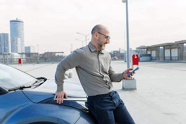 istock Relaxed man leaning on his car while using a smartphone outdoors 2233001980