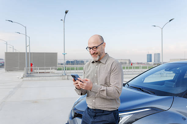 istock Smiling man using smartphone by parked car on rooftop under clear sky 2233002028