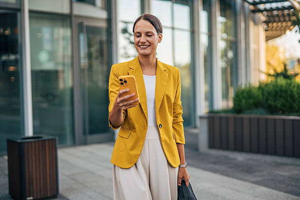 istock Smiling businesswoman using smartphone while walking near office building 2233005446