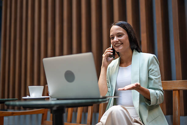 istock Businesswoman working remotely from a cafe, talking on phone and using laptop 2233005502