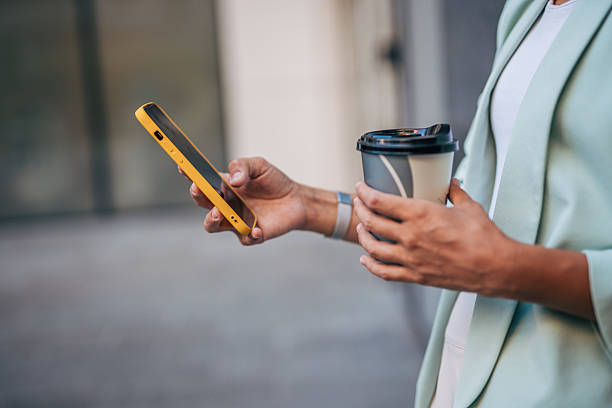 istock Businesswoman using smartphone and holding coffee outside office 2233006257