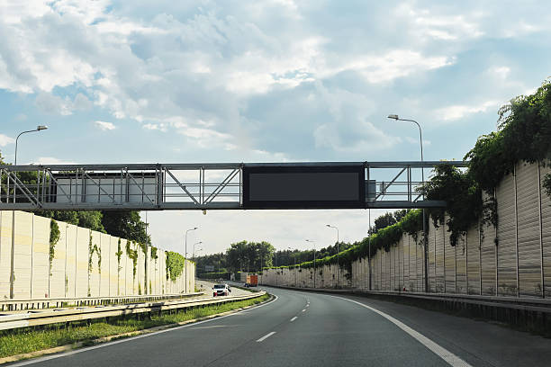 istock Empty highway road with sound barriers and electronic sign above. Modern motorway infrastructure with lanes curving under cloudy sky. 2233006652