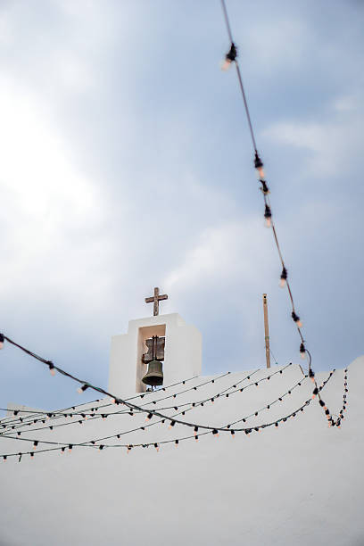 A picturesque view of a white church with a cross, set against a stunning cloudy sky and adorned with decorative string lights in Sant Francesc Xavier little church in Formentera, Spain.
