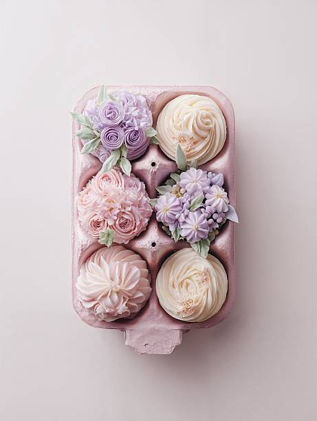 A box filled with six exquisite cupcakes showcases intricate floral designs crafted from icing. The cupcakes feature soft pastel colors such as pink