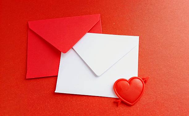 Red paper envelope with blank note mockup inside and Valentines heart on color background. Flat lay, top view. Romantic love letter for Valentine's day concept.