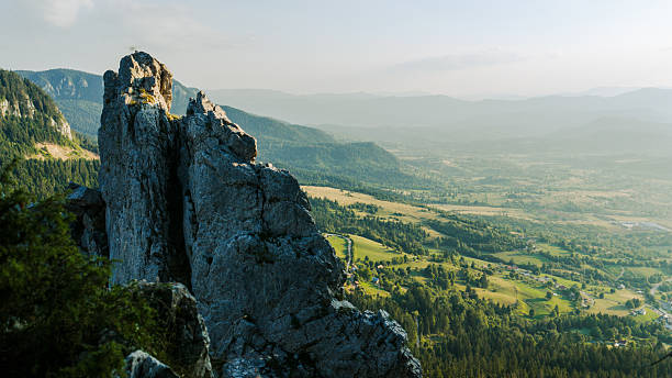 Vertical rocks dominate the mountain edge, overlooking a green valley under clear evening sky