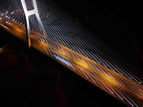 istock Illuminated suspension bridge at night with light trails and distant city lights 2233065075
