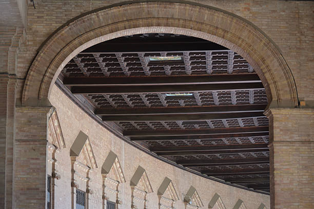 istock A detailed shot captures a large, rounded brick archway, looking into an interior space. The ceiling is a dark, intricate pattern of wood beams. A curved wall with smaller triangular arches is visible below. 2233066882