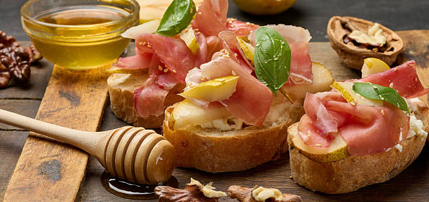 istock Italian bruschetta with prosciutto, pear slices, cream cheese and fresh basil, garnished with sesame seeds 2233067621