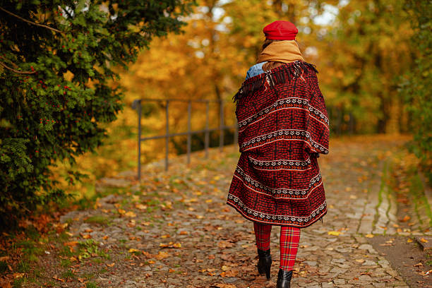 Hello autumn. Seen from behind woman in red hat with scarf walking in the city park.