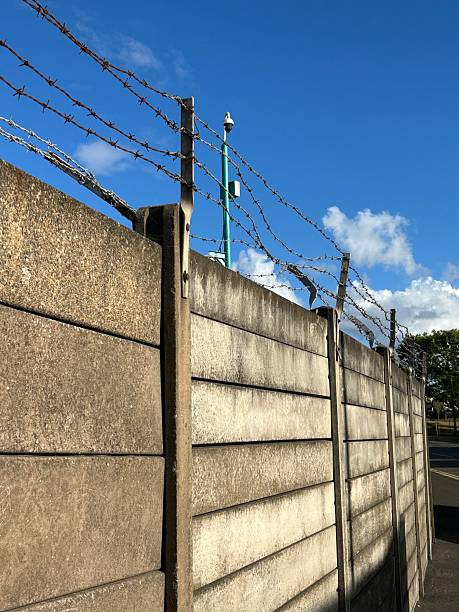 istock Barbed Wire Fence Against Clear Blue Sky with Security Camera in background 2233070810