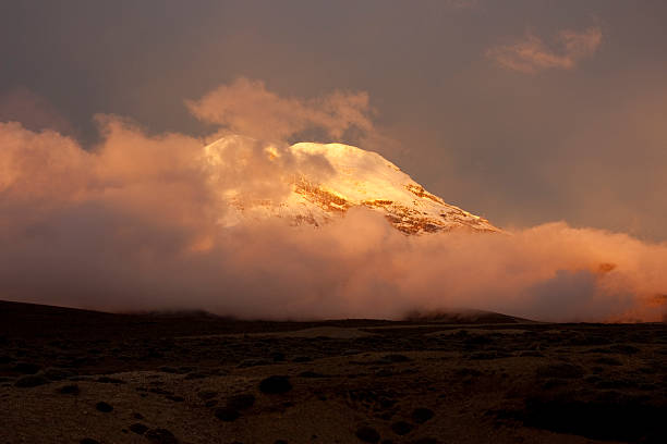 Majestic Chimborazo volcano rising dramatically in the Ecuadorian Andes, bathed in the warm glow of the setting sun, surrounded by soft clouds and breathtaking scenery