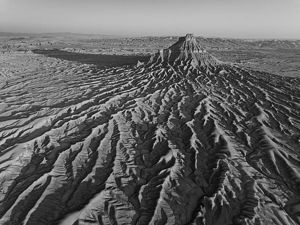 Aerial black-and-white photograph of Factory Butte, Utah, emphasizing the dramatic erosion patterns, textures, and sweeping desert shadows of the badlands.
