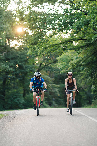 istock Couple cycling on a road through green trees at sunset 2233083213