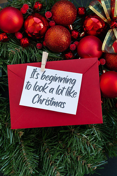 istock IT'S BEGINNING TO LOOK A LOT LIKE CHRISTMAS text on postcard with RED envelope on handmade Christmas wreath. Zero waste eco-friendly Christmas. Sustainable greeting card 2233083851