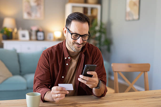istock Cheerful man holding payment card at stylish home workspace 2233087427