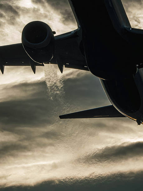 Silhouetted passenger airplane photographed mid-flight on take-off, showing condensation vapor trail behind its powerful engine.