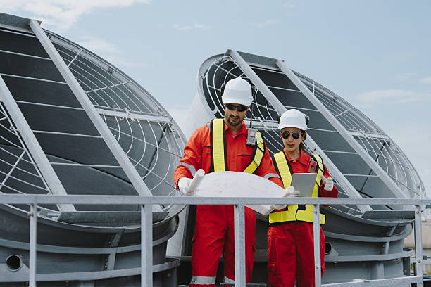 istock Industrial engineers working as a team, maintaining pipes, valves, air conditioning, refrigeration, HVAC systems at construction site. Male technicians in red safety uniforms checking pipe valves. 2233107559
