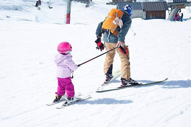 istock Rear view of a father pulling his little daughter with his ski pole on a nice ski day. 2233116740