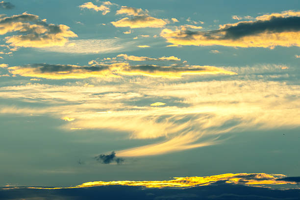 Vibrant colors fill the sky as the sun sets, illuminating fluffy clouds in shades of orange and yellow. The peaceful horizon creates a serene atmosphere perfect for evening relaxation.