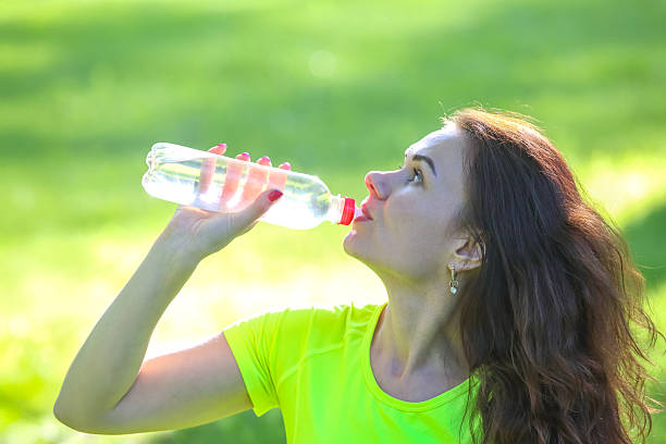 istock Woman drinking water while exercising outdoors in a vibrant green park setting 2233118176
