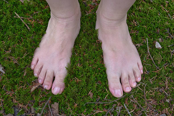 A Human's Bare Feet Resting on a Moss Covered Forest Floor Surrounded by Twigs and Leaves