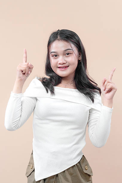 istock A cheerful young Asian woman smiling confidently while pointing upward with both hands, symbolizing new ideas, creativity, inspiration, and a positive outlook in daily life or business. 2233122528