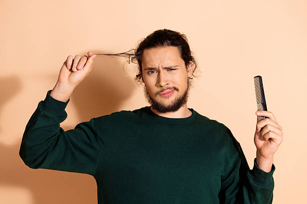 istock Confused man with dark hair holding a comb makes a funny expression against a beige background 2233123232