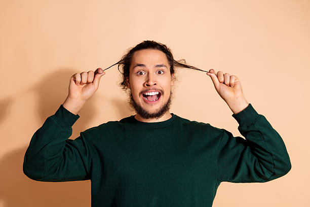 istock Young man with long hair making expressive gestures against a beige background wearing a dark green pullover 2233123263