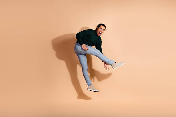 istock Young man in a green casual pullover jumping energetically against a beige background showing emotion and playfulness 2233123441