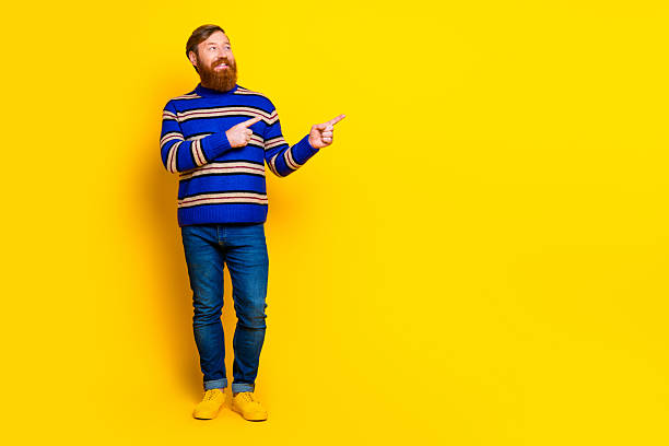 istock Cheerful young red haired man in a vibrant outfit gesturing confidently on a yellow background for casual advertising 2233123752