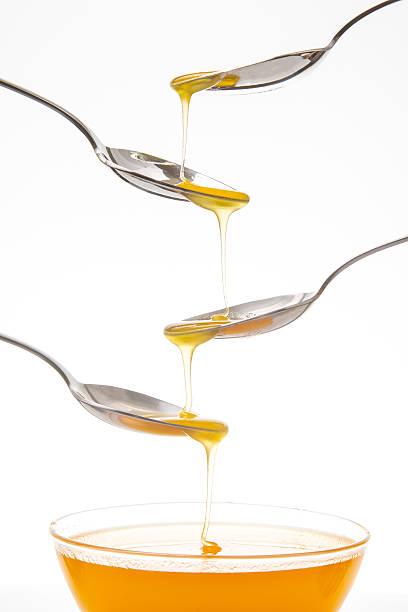 istock Four spoons dripping honey into a glass bowl on a white background 2233124630