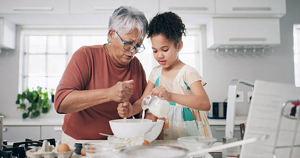 istock Baking, bowl and grandma with child in kitchen for learning, teaching and helping for cookies. Family, home and grandmother with girl with milk, ingredients and bonding for dessert, cake and pastry 2233125523
