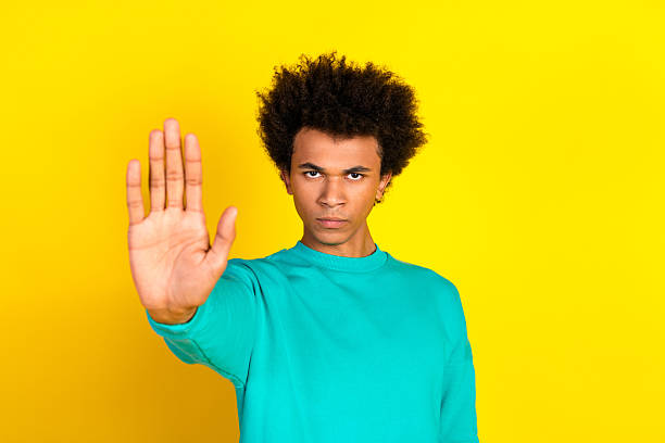 istock Confident young man gesturing stop with open hand on vibrant yellow background wearing teal sweatshirt 2233125982