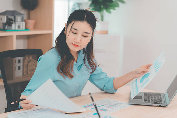 istock Young Asian woman accountant analyzing documents in office sitting at table reading documents Analyze graphs working on company projects. 2233130296