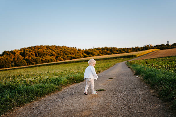 A 22-month-old girl walks independently on a countryside road at golden hour. The wide path and glowing light emphasize freedom, growth, and first steps into independence.