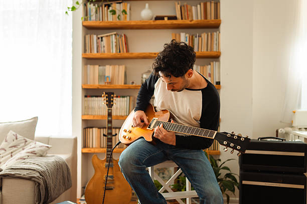 istock Young man practicing guitar at home in cozy living room 2233131007