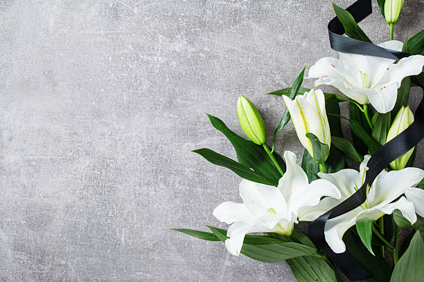 istock White lily bouquet with black ribbon on textured concrete background. Mourning, tribute, condolence, or memorial concept. 2233131009